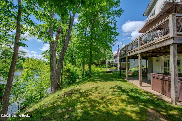 view of grassy yard with a hot tub, a wooden deck, and a patio