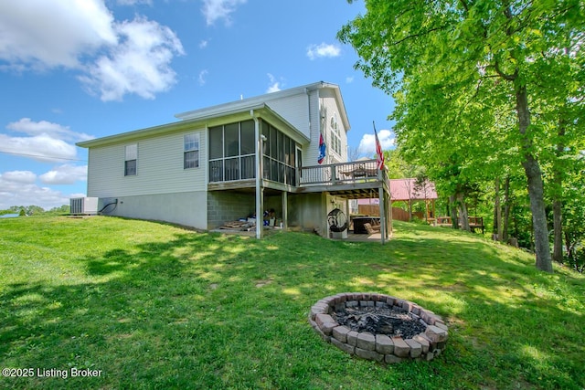 back of house with a sunroom, an outdoor fire pit, a deck, and a lawn