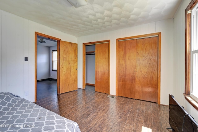unfurnished bedroom with wood finished floors and multiple closets