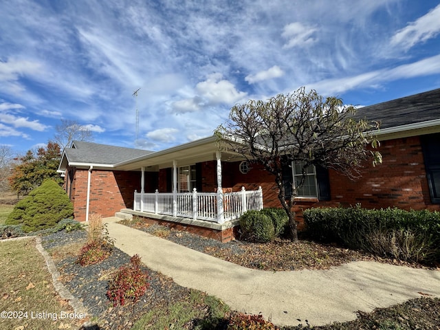 view of side of property featuring a porch, roof with shingles, and brick siding