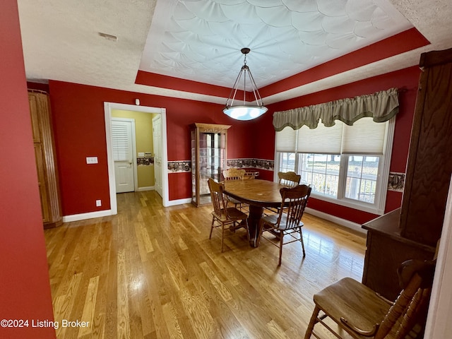 dining area featuring baseboards, a tray ceiling, and light wood-type flooring