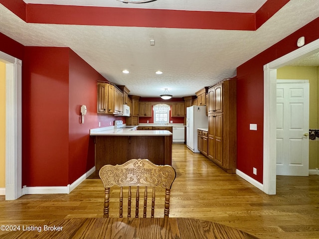 kitchen with baseboards, white appliances, a peninsula, wood finished floors, and light countertops