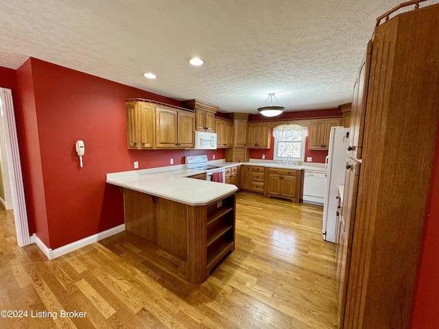 kitchen featuring a sink, a peninsula, a textured ceiling, and white appliances