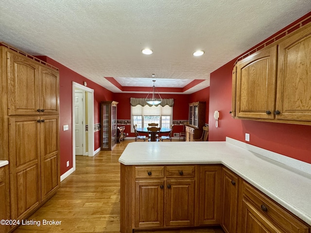 kitchen with a peninsula, brown cabinets, light wood-type flooring, a textured ceiling, and light countertops