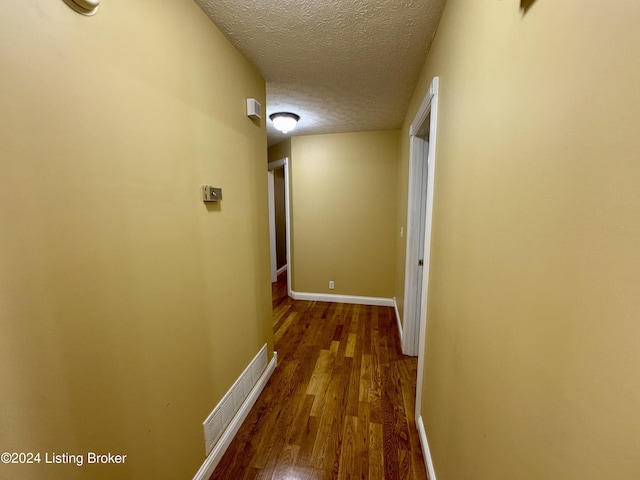 hallway with a textured ceiling, baseboards, and wood finished floors