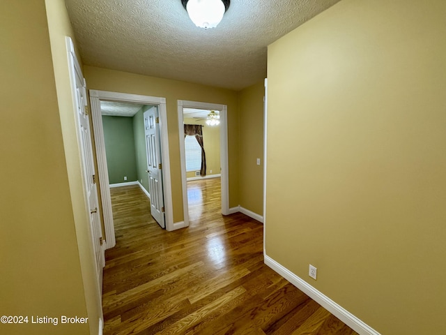 hall featuring a textured ceiling, baseboards, and dark wood finished floors