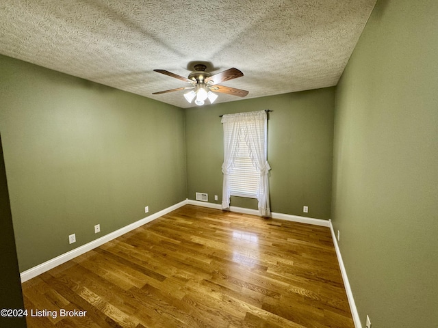 spare room with wood finished floors, a textured ceiling, visible vents, a ceiling fan, and baseboards