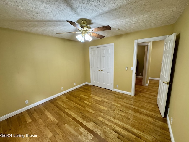 unfurnished bedroom featuring baseboards, a closet, a textured ceiling, and wood finished floors