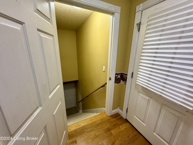 doorway featuring baseboards, light wood-style flooring, and a textured ceiling