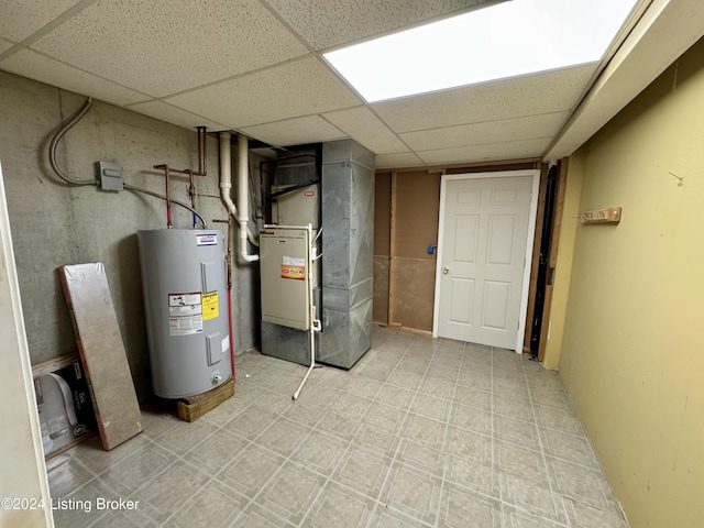 finished below grade area with a drop ceiling, tile patterned floors, heating unit, and electric water heater