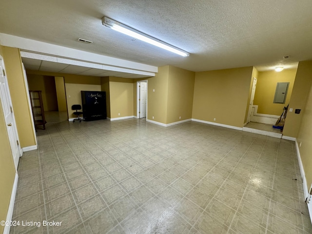 basement featuring electric panel, a textured ceiling, visible vents, and baseboards