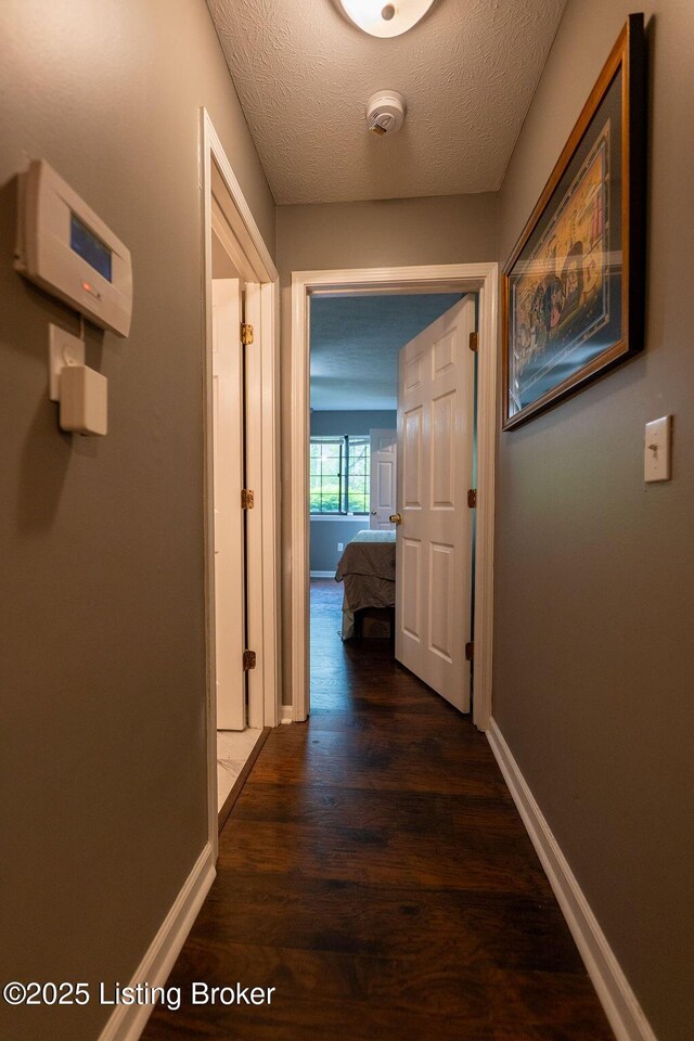hall featuring dark wood finished floors, baseboards, and a textured ceiling