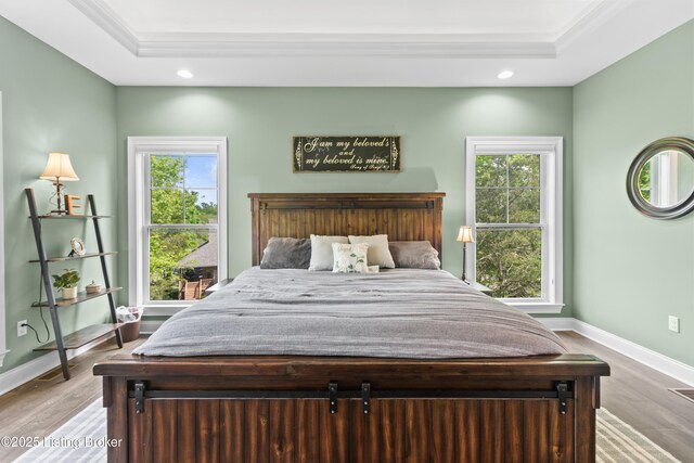 bedroom with a tray ceiling, recessed lighting, wood finished floors, baseboards, and ornamental molding