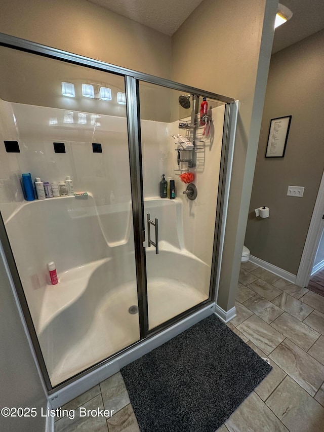 bathroom with a stall shower, toilet, and baseboards