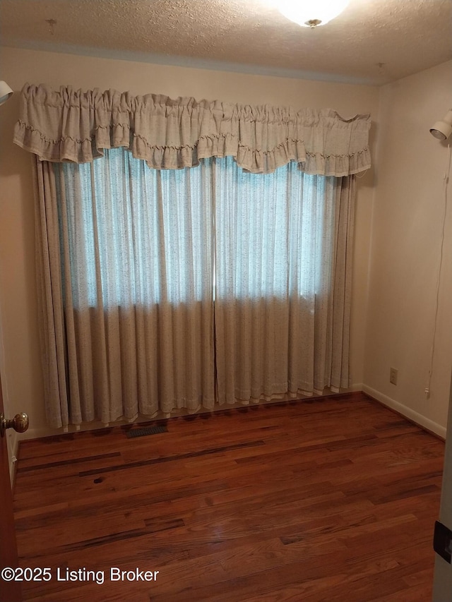 unfurnished room featuring a textured ceiling, baseboards, and wood finished floors