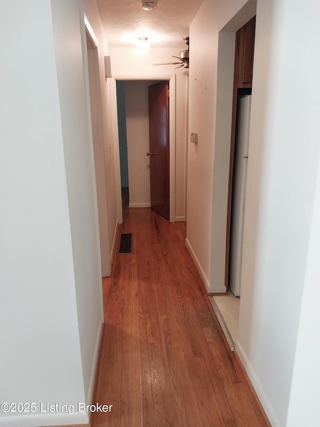 corridor with light wood finished floors, baseboards, and visible vents