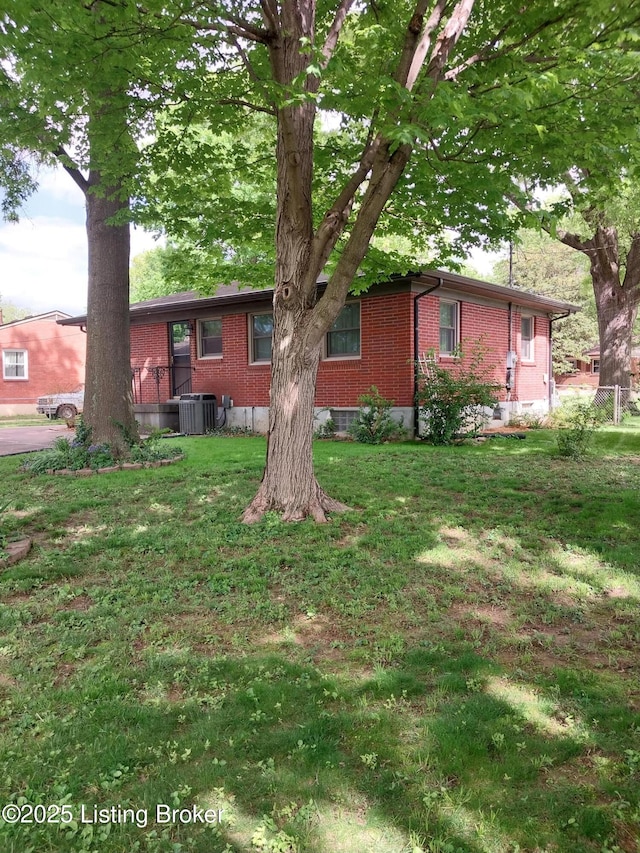 exterior space featuring a yard, brick siding, and central AC