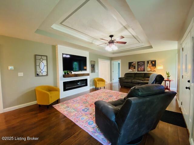 1300 Midway Ln, Springfield, KY 40069 - living area featuring a raised ceiling, dark wood-style floors, baseboards, ceiling fan, and a glass covered fireplace