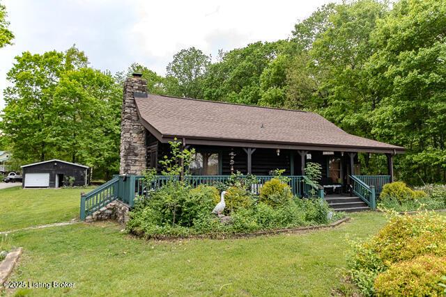 view of front of property with a chimney, a front yard, covered porch, and a detached garage