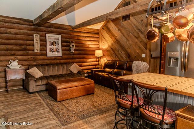 interior space with log walls, wood finished floors, and beamed ceiling