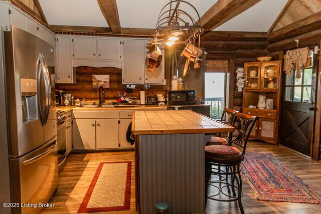 kitchen with stainless steel fridge, tile counters, light wood-type flooring, rustic walls, and black microwave