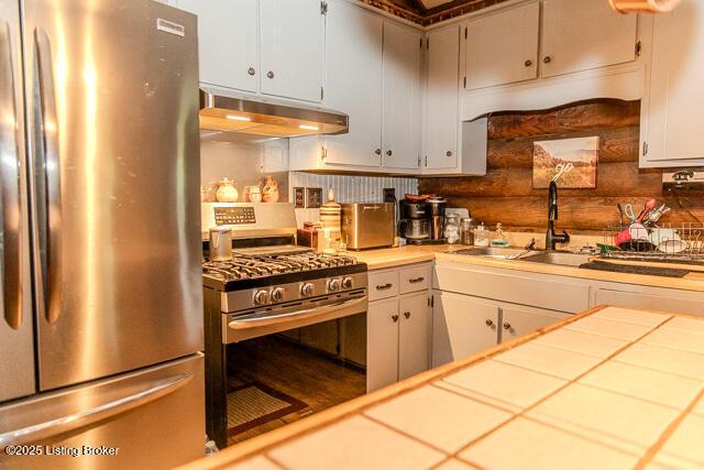 kitchen featuring under cabinet range hood, a sink, white cabinetry, tile counters, and appliances with stainless steel finishes