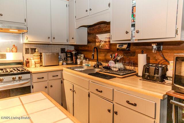 kitchen featuring gas range, light countertops, decorative backsplash, and under cabinet range hood