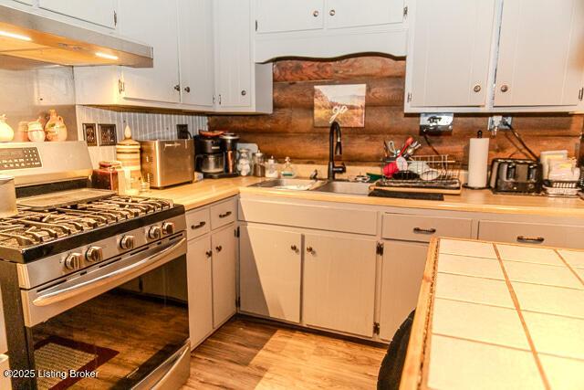 kitchen featuring a sink, tile countertops, light wood-type flooring, under cabinet range hood, and gas stove