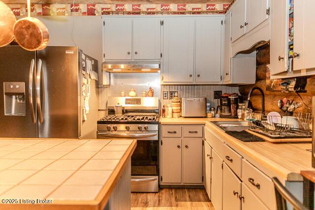 kitchen with a sink, stainless steel appliances, light wood-type flooring, under cabinet range hood, and tile counters