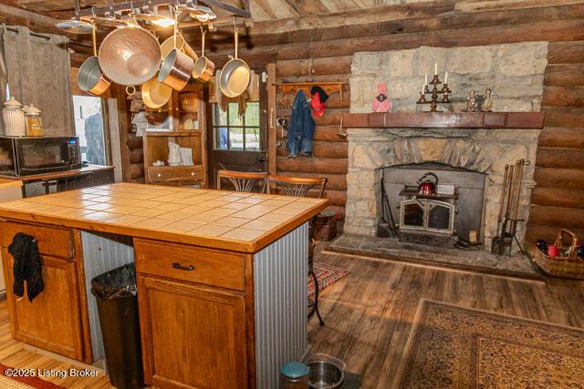 kitchen with brown cabinetry, log walls, black microwave, wood finished floors, and tile counters