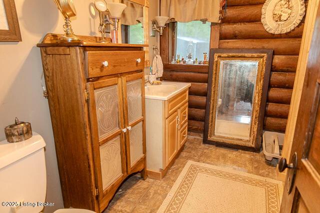 bathroom with toilet, rustic walls, and vanity