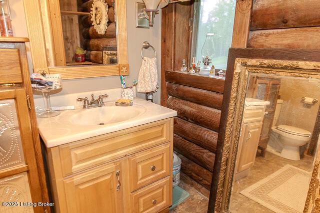 bathroom with toilet, log walls, and vanity