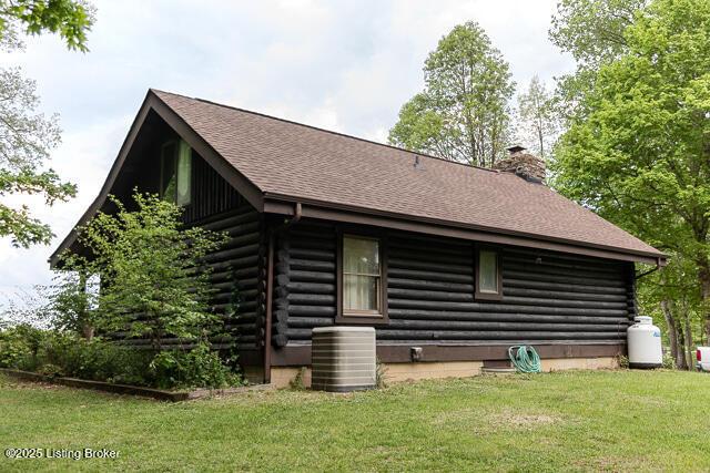 back of house with a lawn, a chimney, cooling unit, log exterior, and a shingled roof