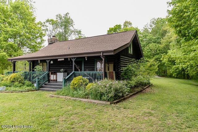 view of front of property featuring covered porch, a chimney, log exterior, and a front yard