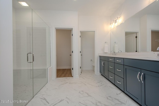full bathroom featuring double vanity, toilet, a stall shower, a sink, and marble finish floor