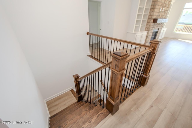 stairway featuring wood finished floors, baseboards, and a fireplace