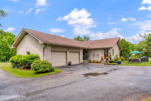 view of front of house with brick siding, an attached garage, asphalt driveway, and roof with shingles