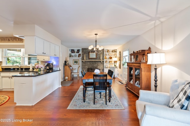dining room with a chandelier, dark wood-style floors, built in shelves, and a fireplace