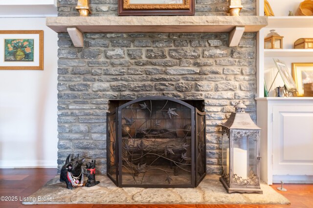detailed view of a fireplace with raised hearth, wood finished floors, and baseboards