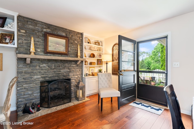 living area with wood finished floors, a stone fireplace, built in shelves, and baseboards
