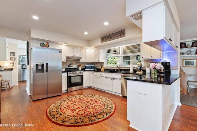 kitchen featuring stainless steel appliances, under cabinet range hood, a sink, a peninsula, and white cabinets