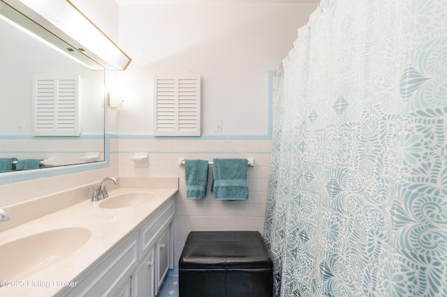 bathroom with tile walls, wainscoting, and double vanity