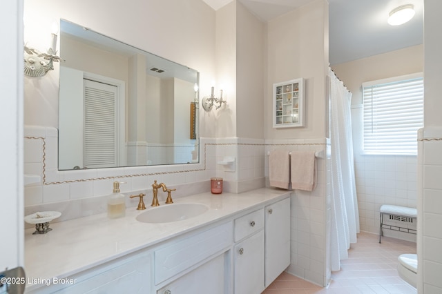 bathroom with tile walls, vanity, tile patterned flooring, a wainscoted wall, and toilet