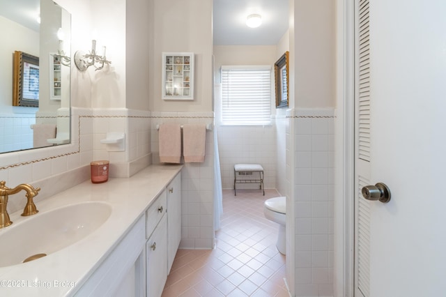 bathroom with tile walls, tile patterned flooring, wainscoting, vanity, and toilet
