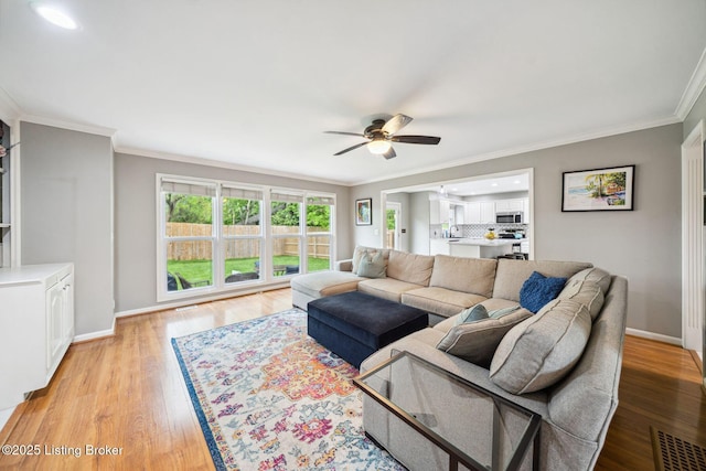 living area featuring ceiling fan, ornamental molding, baseboards, and light wood finished floors