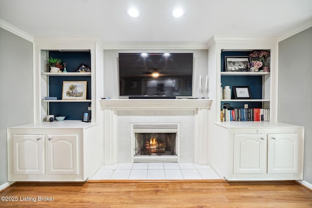unfurnished living room featuring ornamental molding, built in features, a tiled fireplace, and wood finished floors