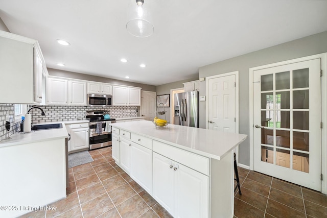 kitchen featuring appliances with stainless steel finishes, a sink, a center island, light countertops, and white cabinets