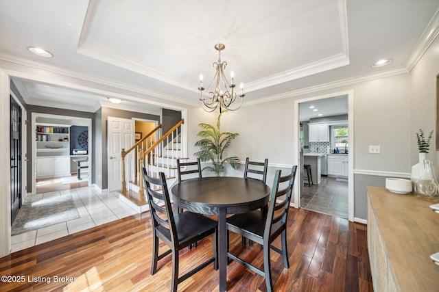 dining room with a chandelier, crown molding, wood-type flooring, stairway, and a tray ceiling