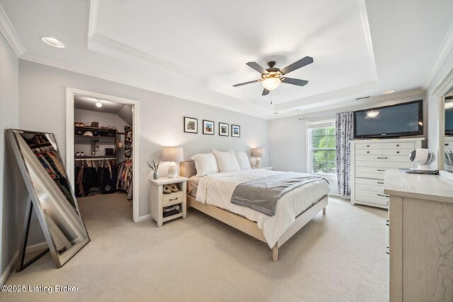 bedroom with a raised ceiling, crown molding, a walk in closet, light colored carpet, and a ceiling fan