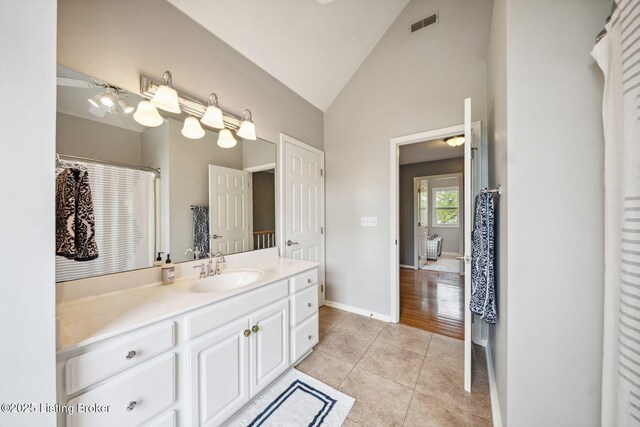 bathroom with tile patterned flooring, vanity, baseboards, and high vaulted ceiling